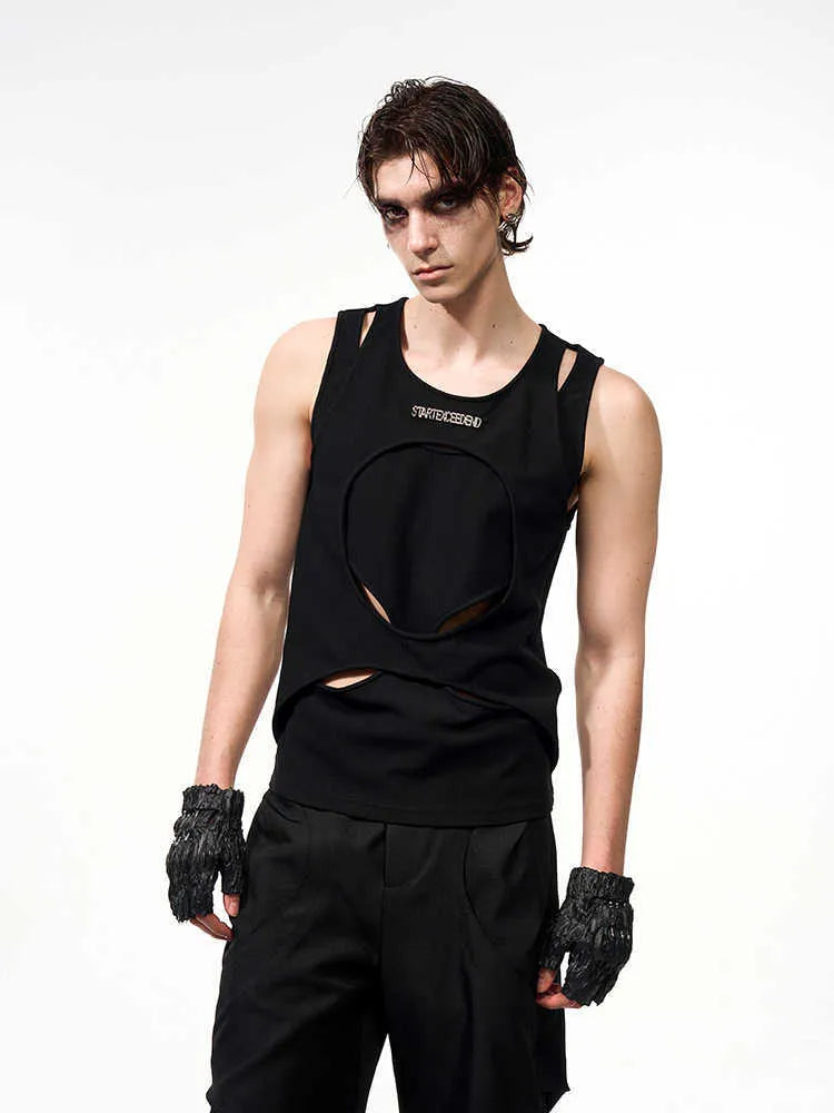 Man wearing a loose-fitting black sleeveless waistcoat with a round neck over a white t-shirt.