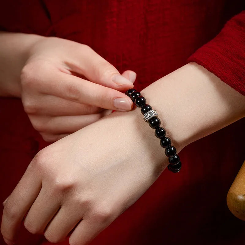 Obsidian bead bracelet with a hand-carved zodiac animal and bodhisattva charm on a wrist.