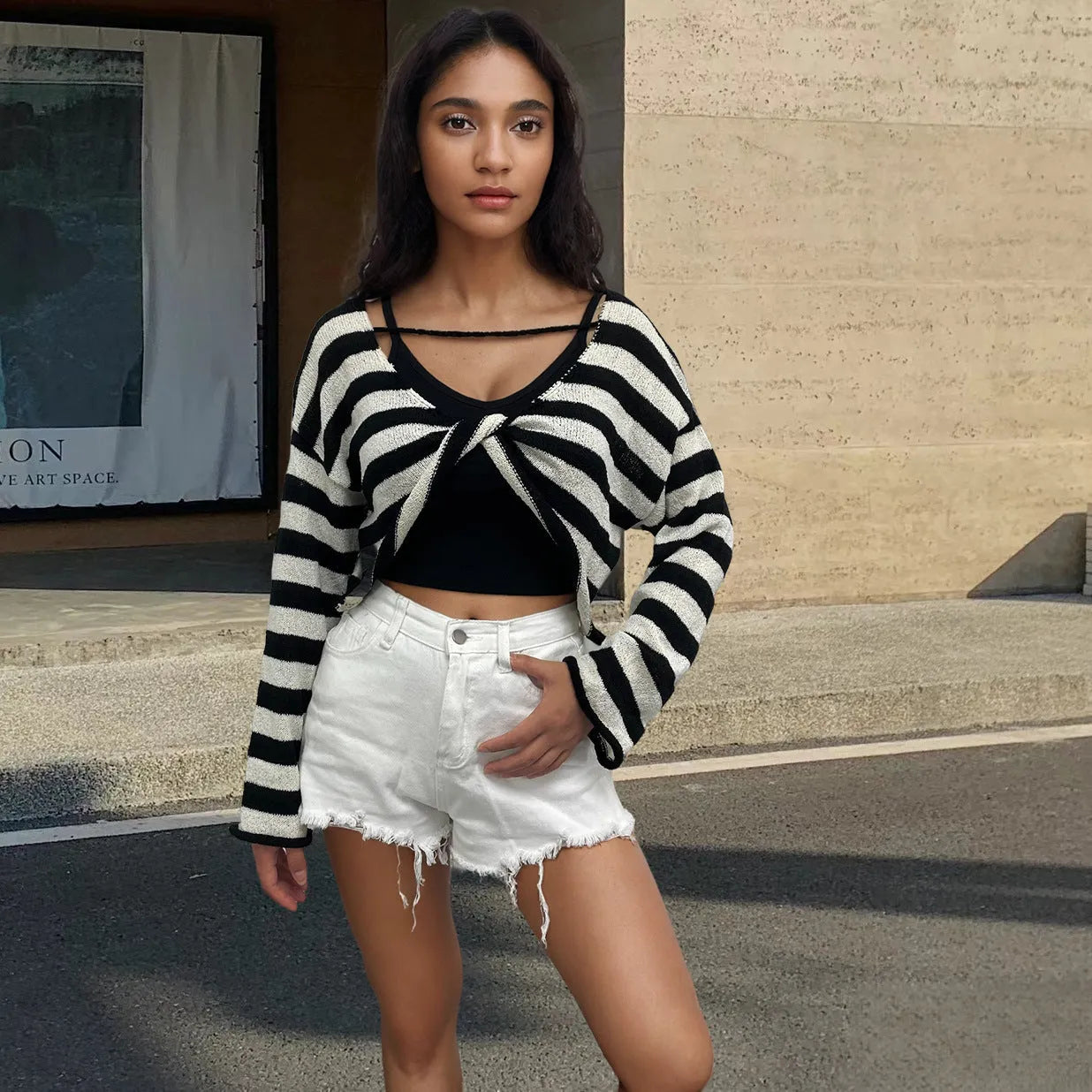 A woman wearing a cropped black and white striped long-sleeved sweater with a front and back exposed-navel design.