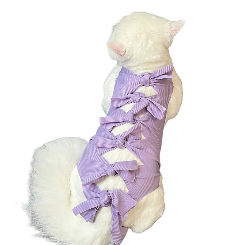 A pink lace-up cat recovery suit on a grey cat, showing the back closure and full-body fit.
