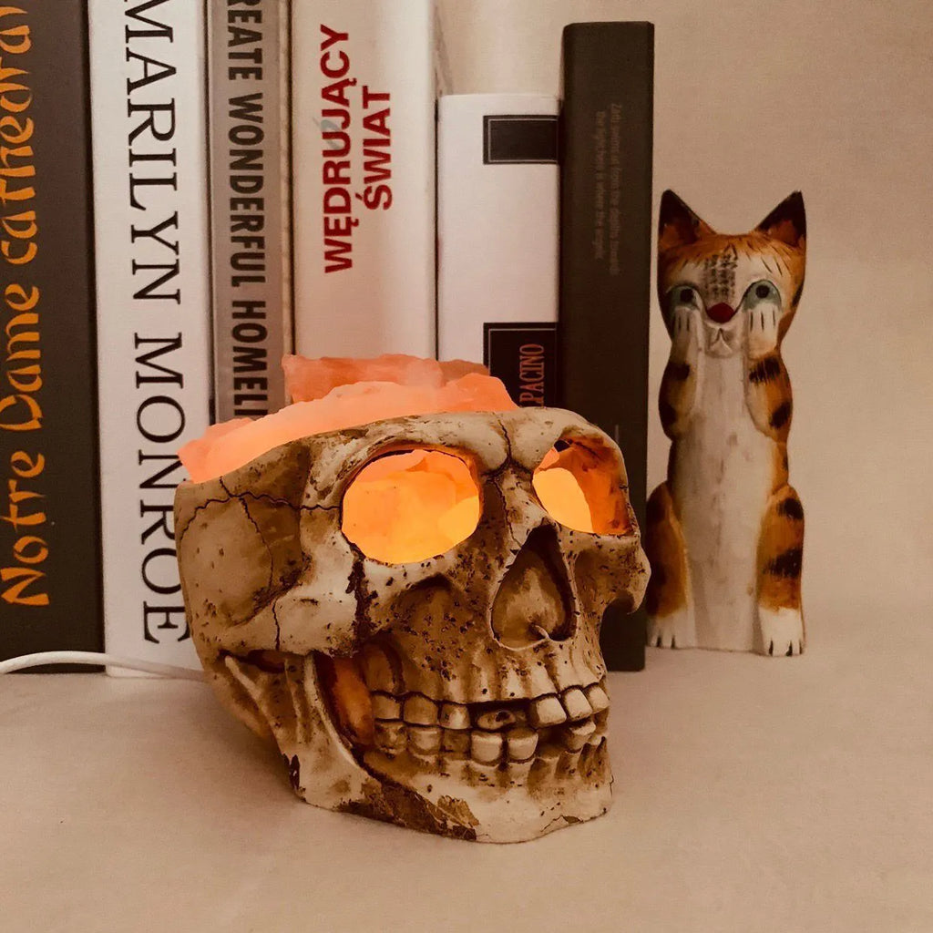 Skull-shaped Himalayan crystal salt lamp with USB dimmable LED showing warm amber light on a resin base