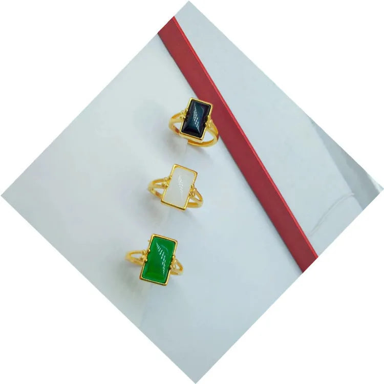 Adjustable gold-plated brass ring with a coloured gemstone inlay on a plain background.