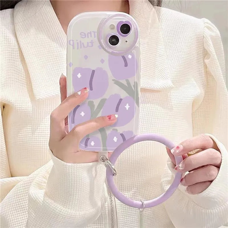 Clear purple tulip printed iPhone case with attached adjustable wrist strap on a table.