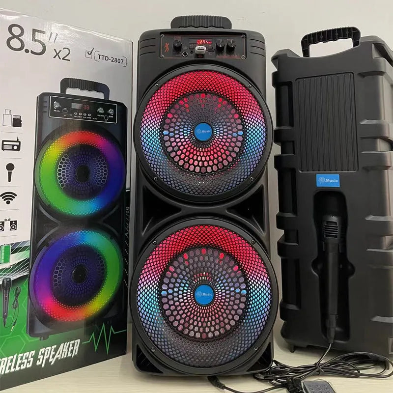 Black portable Bluetooth speaker with double 8-inch speakers, wired microphone, and remote control on a table