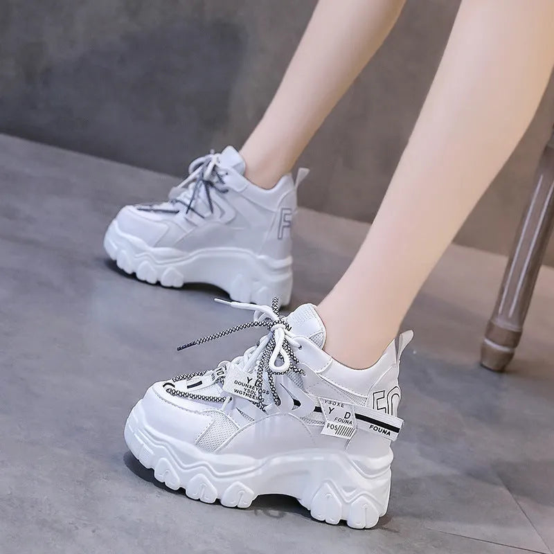 White women's low-top platform sports trainers with mesh panels and a black cross-strap on a rubber sole.