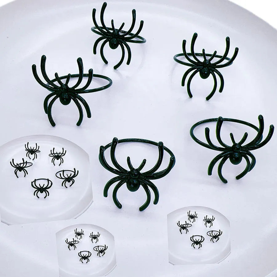 Six black alloy spider-shaped napkin rings on a dark table, showing detailed legs and a 5cm height.