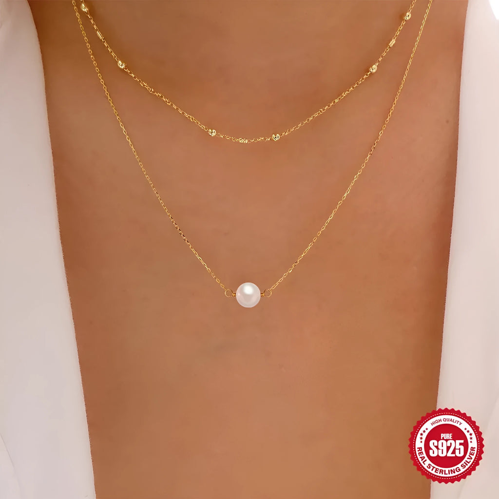 Close-up of a double-layer sterling silver necklace with twin pearl geometric pendants on a ball bead chain.