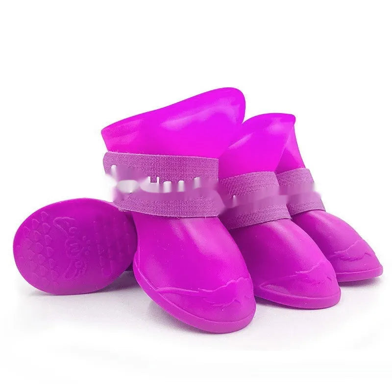 Set of four soft-soled rubber rain shoes for dogs in various colours on a wet surface.