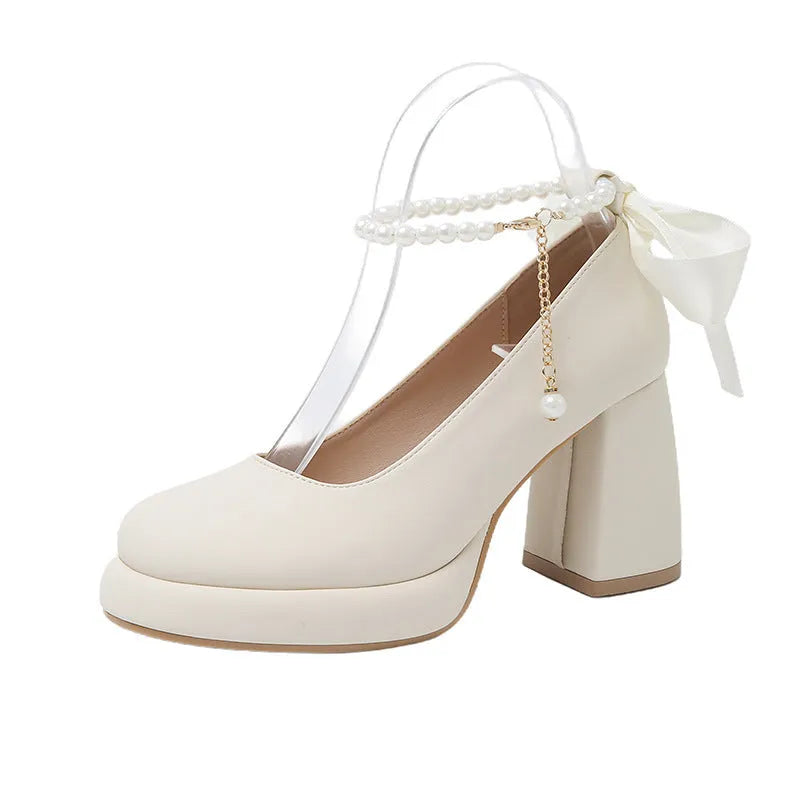 Women's beige Mary Jane shoes with chunky heel and silver ankle strap buckle on a wooden floor.