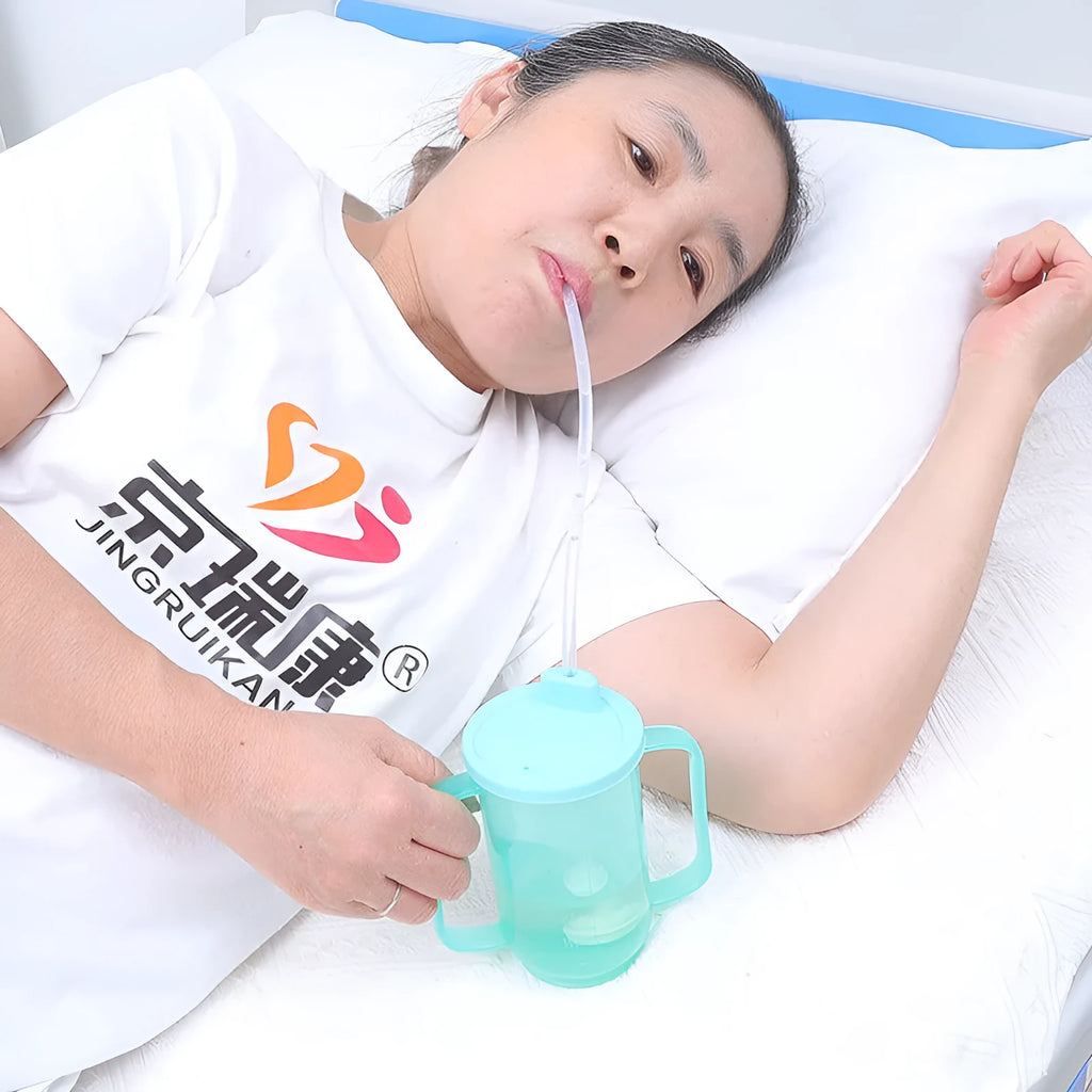 Oblique mouth choke-proof drinking cup with handle and lid, shown in bed care setting.