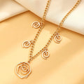 Gold spiral donut pendant necklace, matching bracelet and ear hooks set on a grey background.