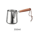 Stainless steel milk frothing cup with wooden handle showing interior measurement scale markings