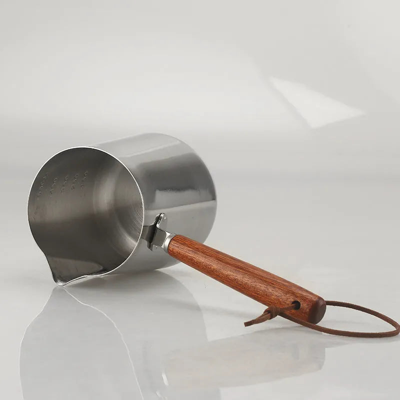 Stainless steel milk frothing cup with wooden handle showing interior measurement scale markings