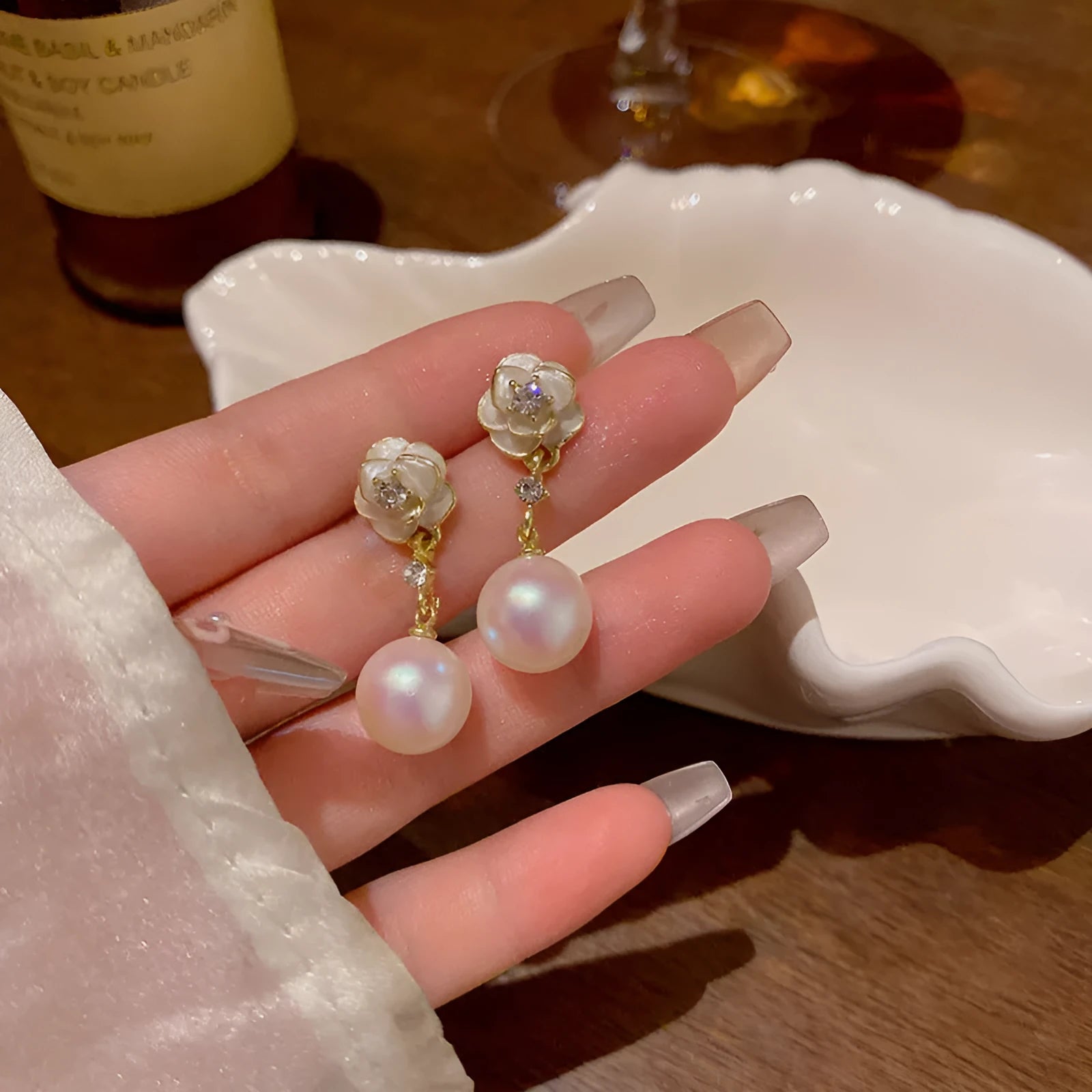 Gold-tone camellia flower stud earrings with a white crystal pearl in the centre on a white background.
