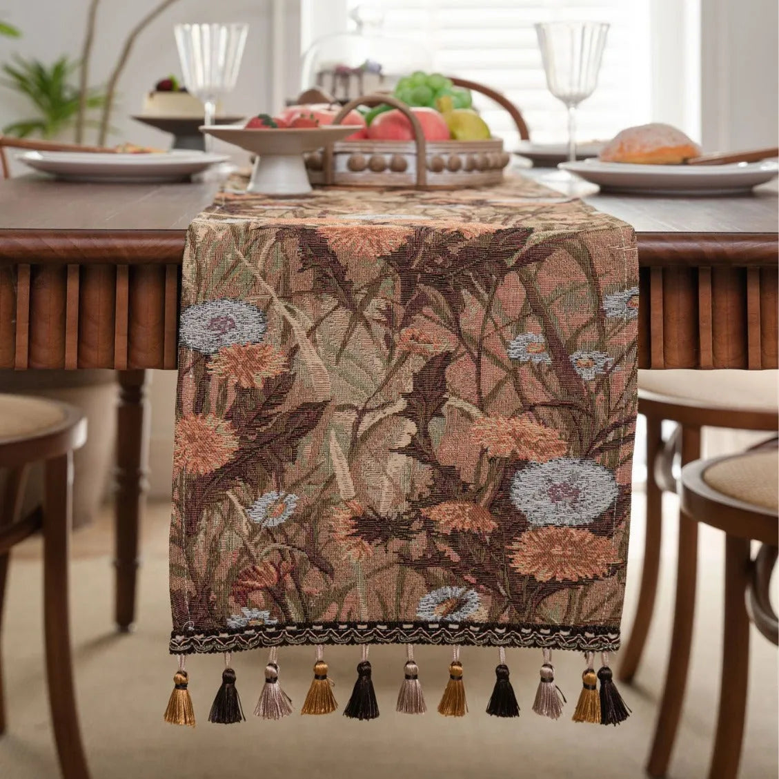 Long beige jacquard table runner with floral pattern and knotted tassels on a wooden dining table.