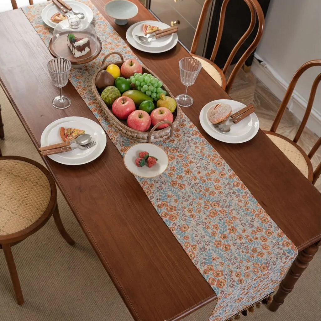 Long beige jacquard table runner with floral pattern and knotted tassels on a wooden dining table.