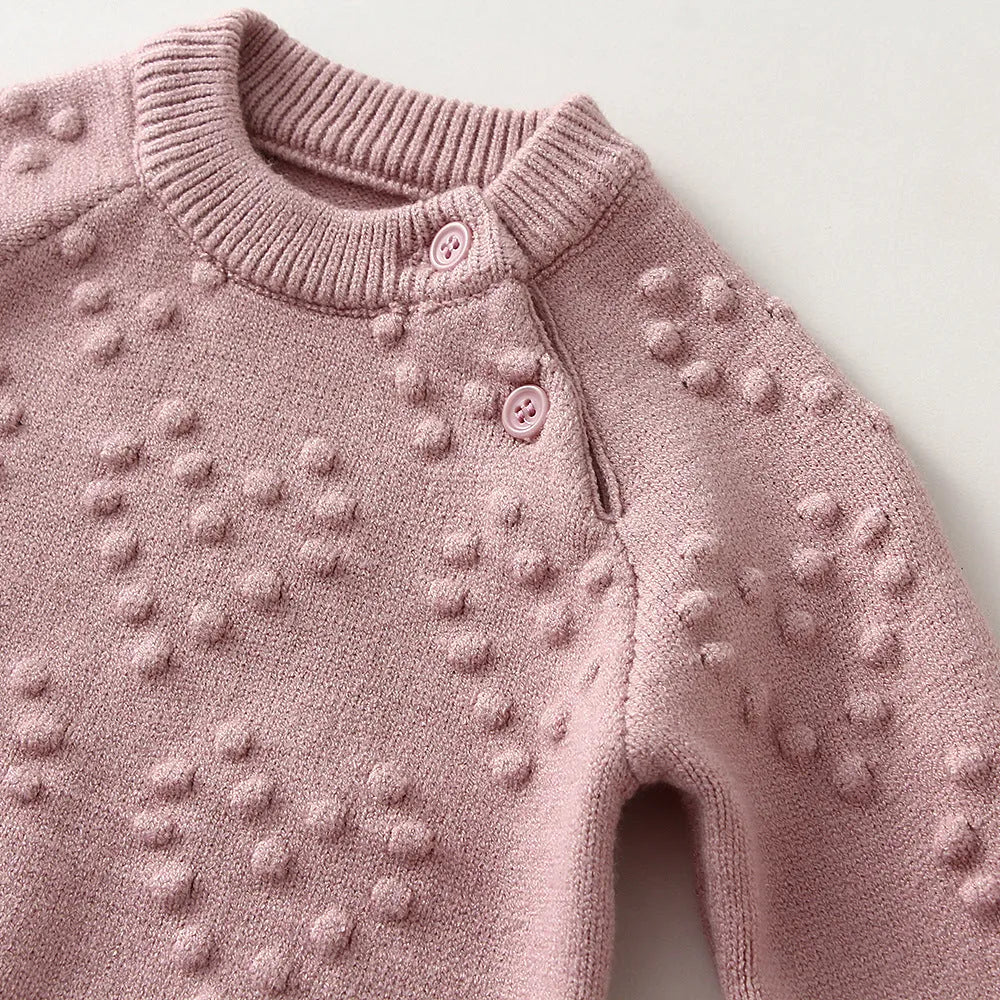 Girl's pink knitted cotton long sleeve sweater and matching pants set on a hanger