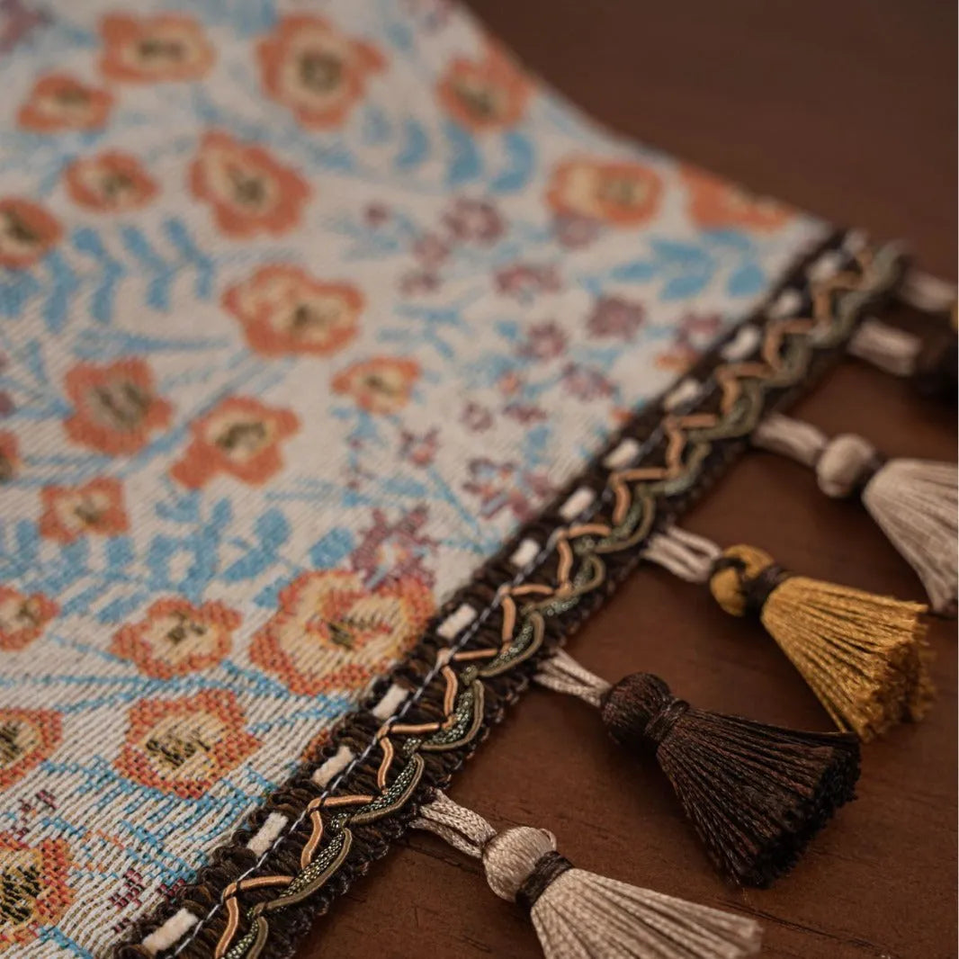 Long beige jacquard table runner with floral pattern and knotted tassels on a wooden dining table.