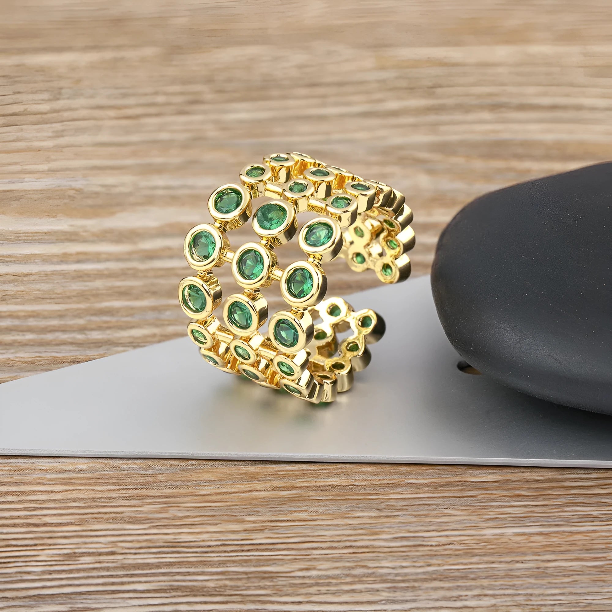 Gold coloured copper ring with green zircon stones set across its wide, layered band.