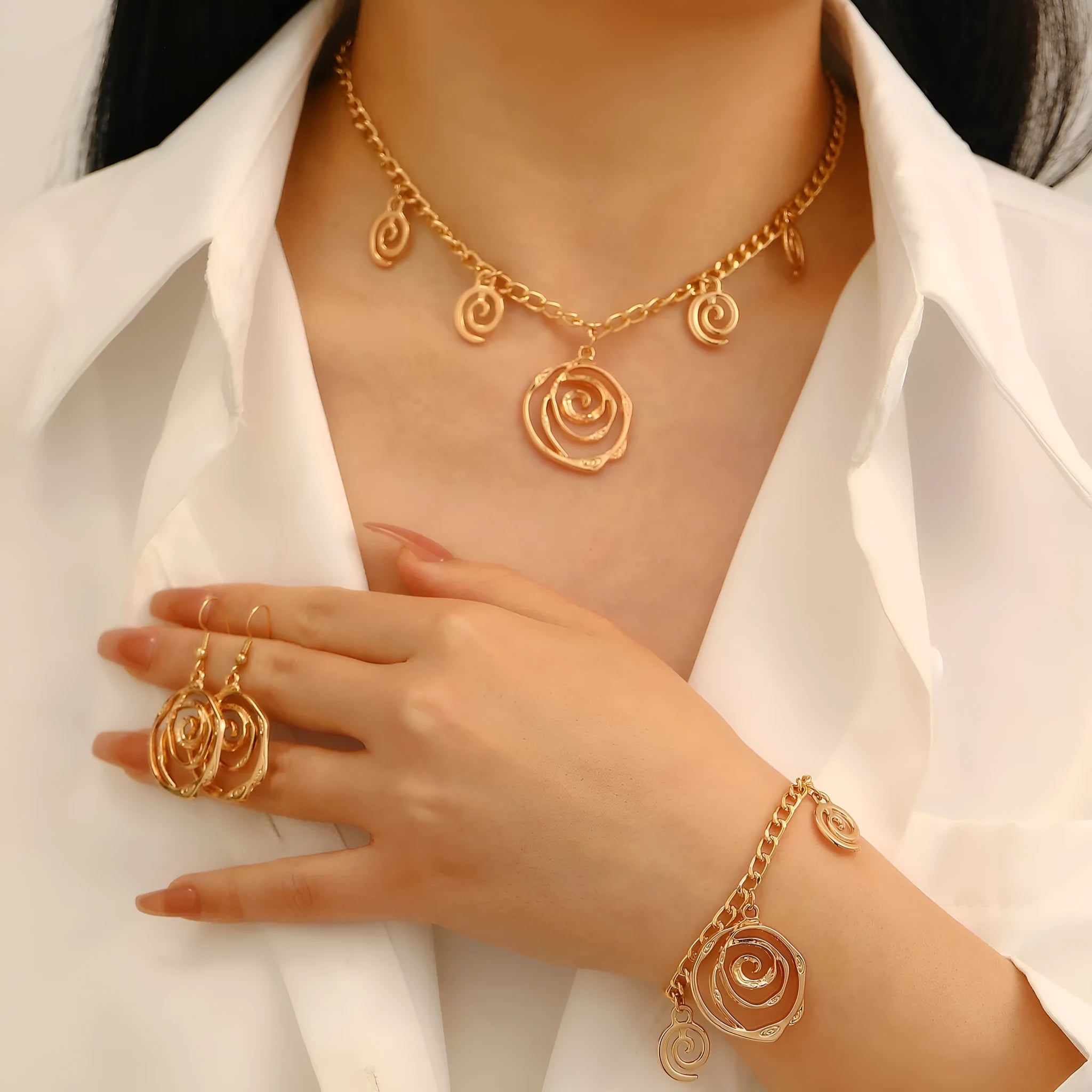 Gold spiral donut pendant necklace, matching bracelet and ear hooks set on a grey background.