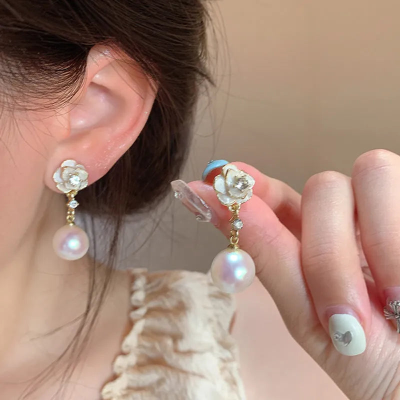 Gold-tone camellia flower stud earrings with a white crystal pearl in the centre on a white background.