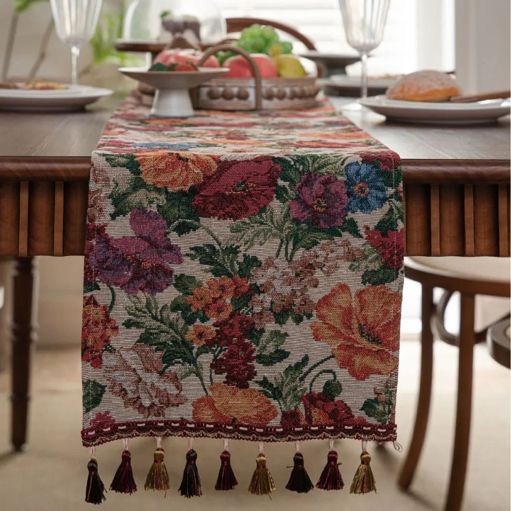 Long beige jacquard table runner with floral pattern and knotted tassels on a wooden dining table.
