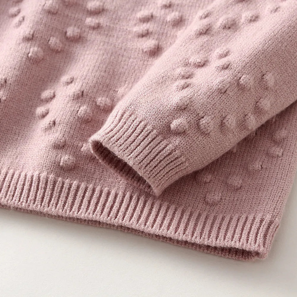 Girl's pink knitted cotton long sleeve sweater and matching pants set on a hanger