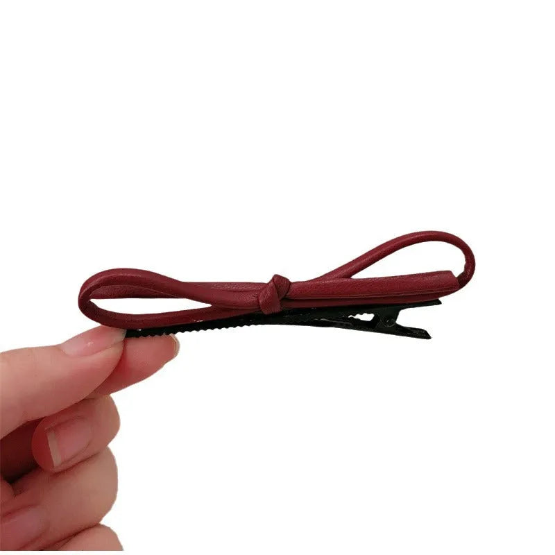 Wine red leather bow hair barrette with a metal clip on a white background