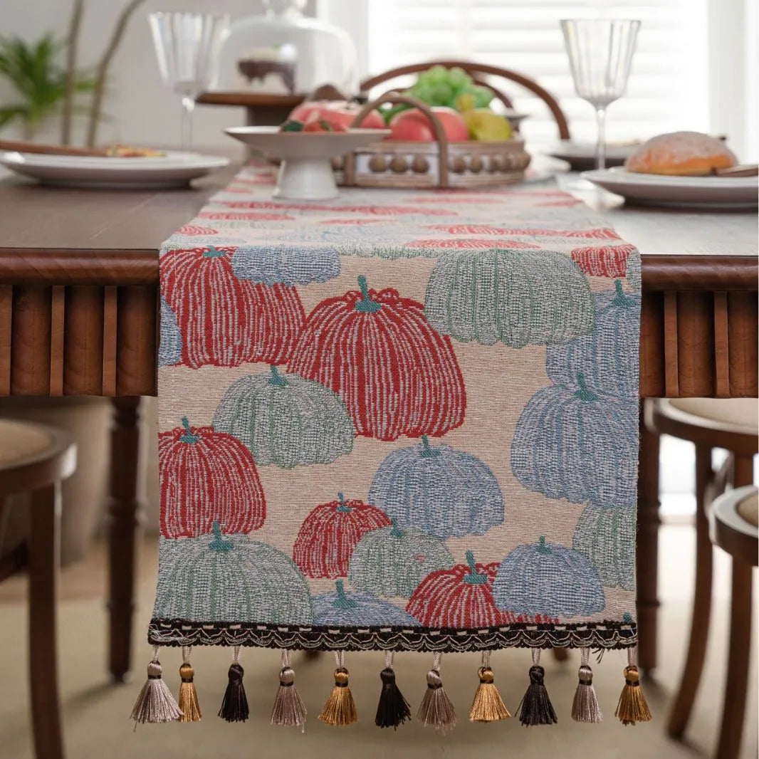 Long beige jacquard table runner with floral pattern and knotted tassels on a wooden dining table.