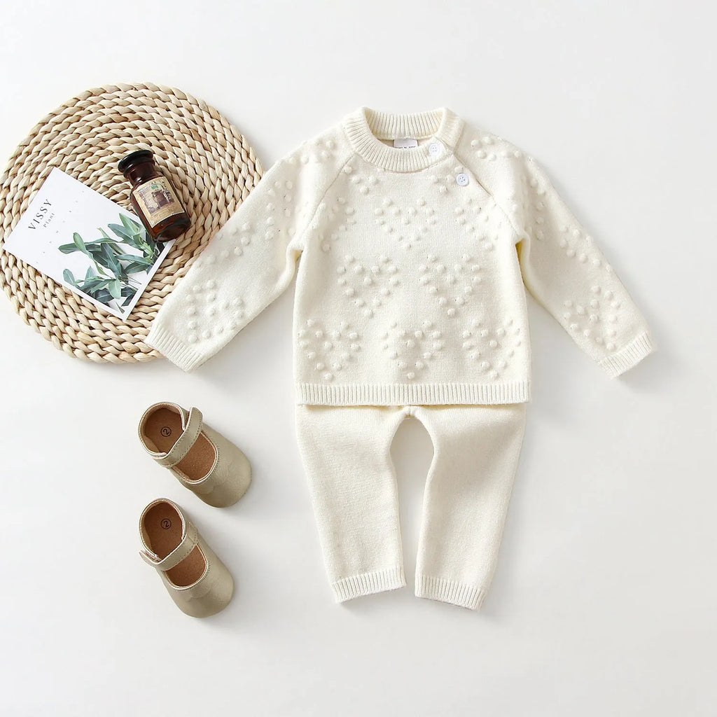 Girl's pink knitted cotton long sleeve sweater and matching pants set on a hanger