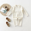 Girl's pink knitted cotton long sleeve sweater and matching pants set on a hanger