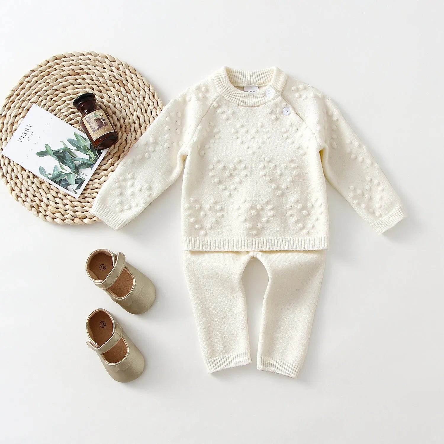 Girl's pink knitted cotton long sleeve sweater and matching pants set on a hanger