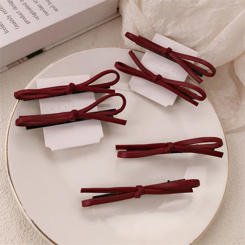 Wine red leather bow hair barrette with a metal clip on a white background