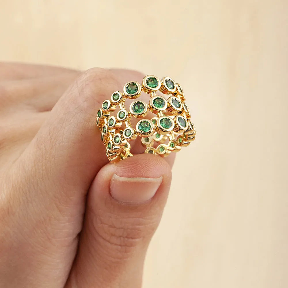 Gold coloured copper ring with green zircon stones set across its wide, layered band.