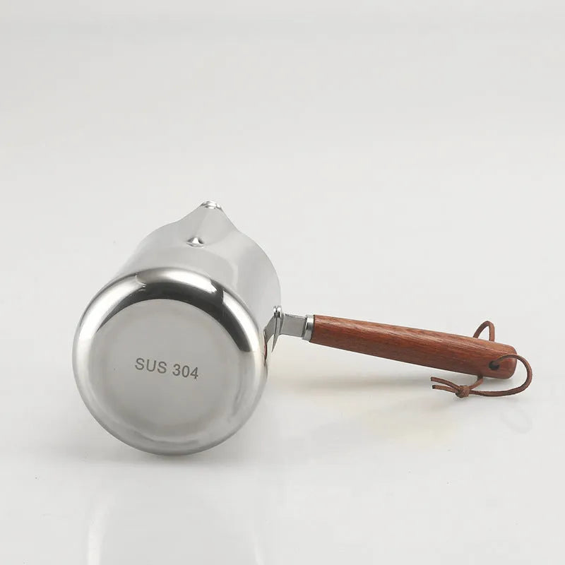 Stainless steel milk frothing cup with wooden handle showing interior measurement scale markings