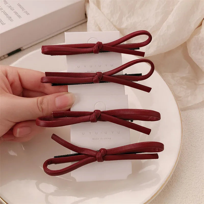 Wine red leather bow hair barrette with a metal clip on a white background