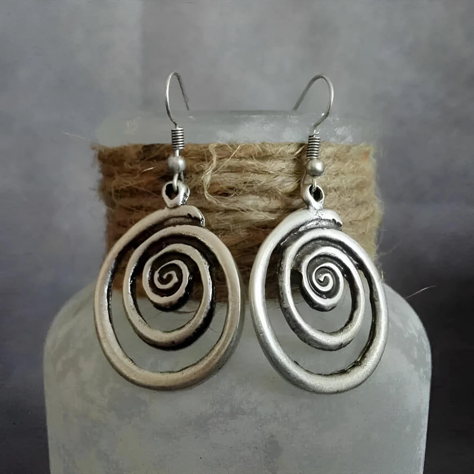 Silver geometric spiral earrings with a distressed texture on a white background.