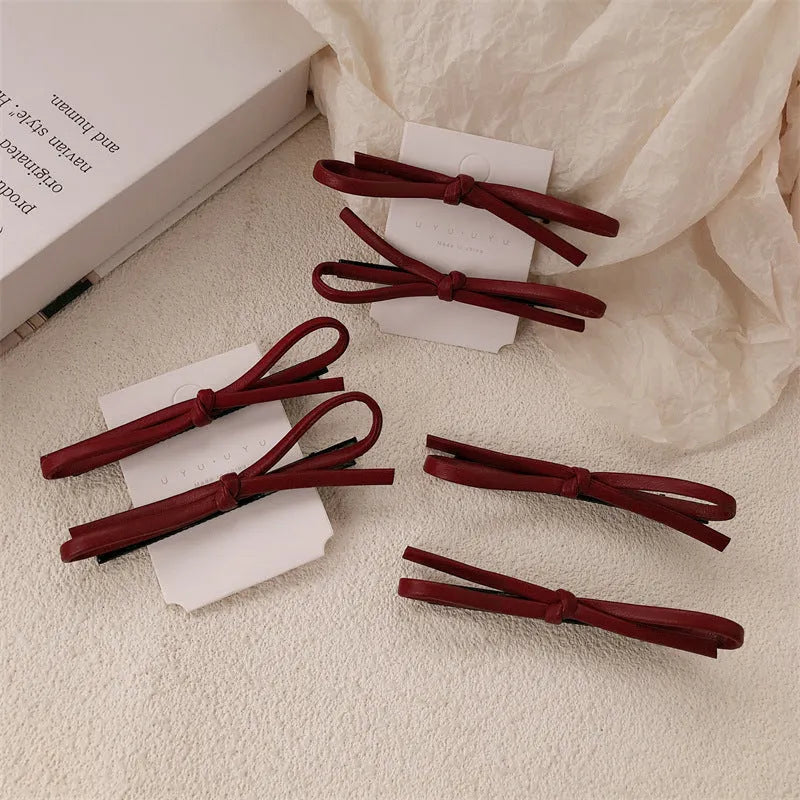Wine red leather bow hair barrette with a metal clip on a white background