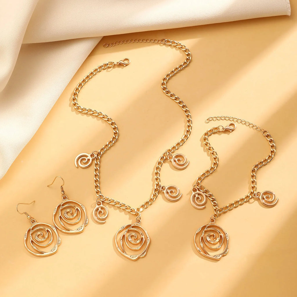 Gold spiral donut pendant necklace, matching bracelet and ear hooks set on a grey background.