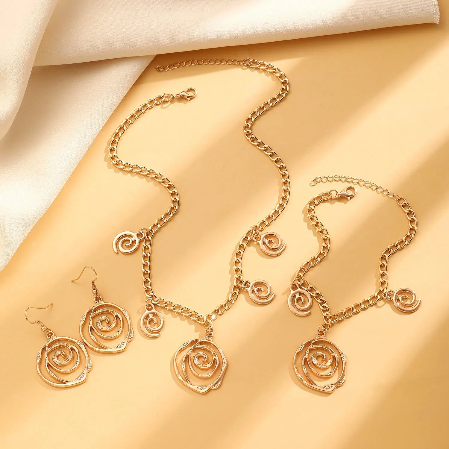 Gold spiral donut pendant necklace, matching bracelet and ear hooks set on a grey background.