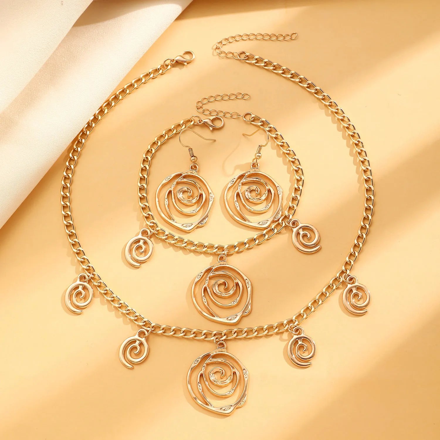 Gold spiral donut pendant necklace, matching bracelet and ear hooks set on a grey background.