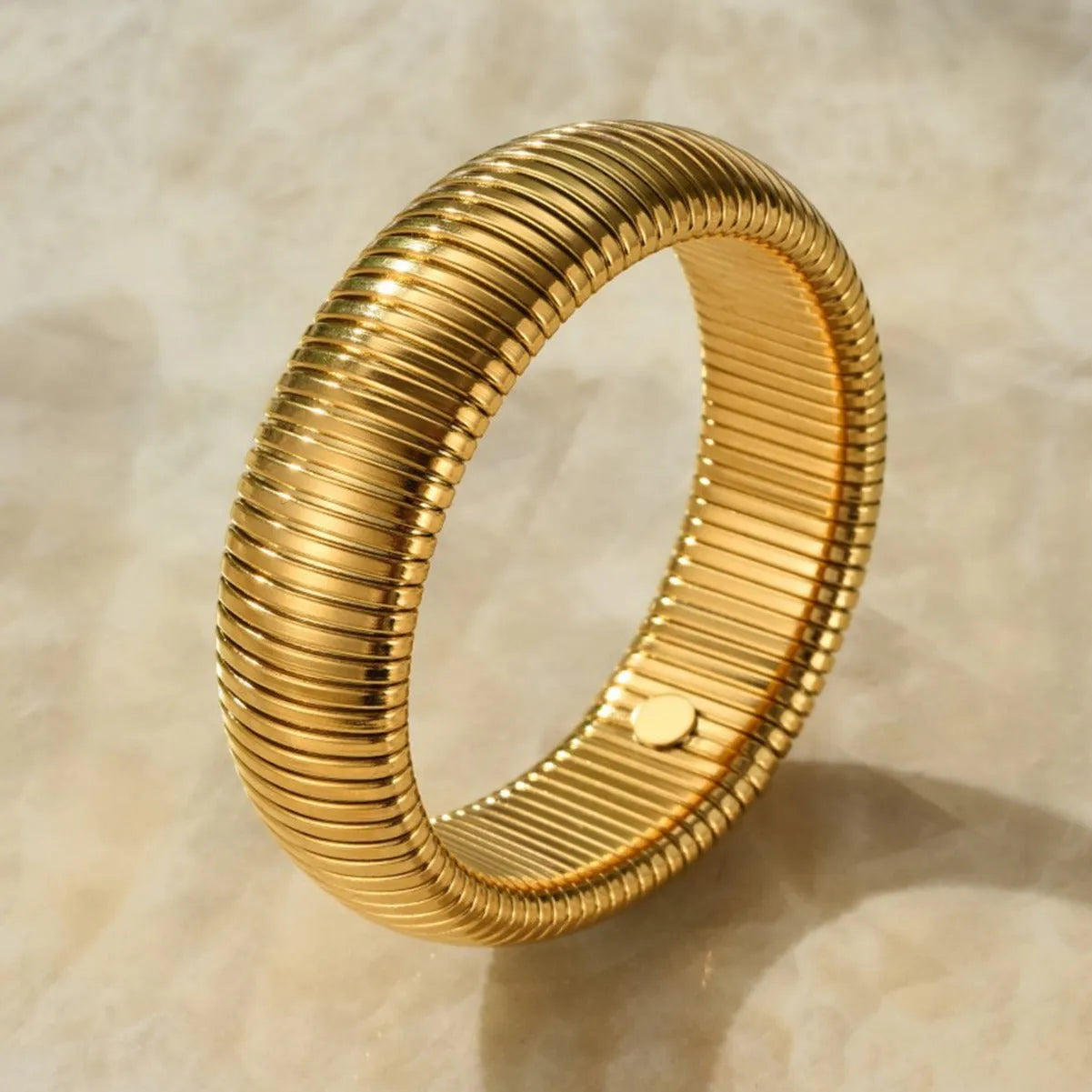 Gold elastic titanium steel bracelet with a wide vertical stripe ring pattern on a wrist.