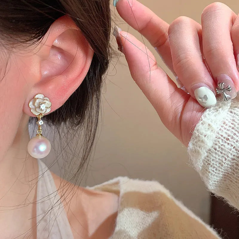 Gold-tone camellia flower stud earrings with a white crystal pearl in the centre on a white background.
