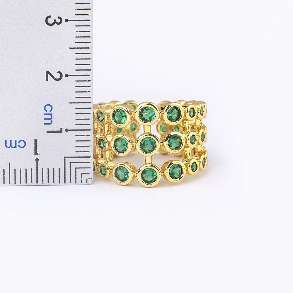 Gold coloured copper ring with green zircon stones set across its wide, layered band.