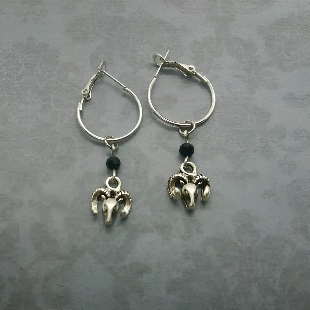 A pair of silver-coloured round hoop earrings with a Tibetan antelope design.