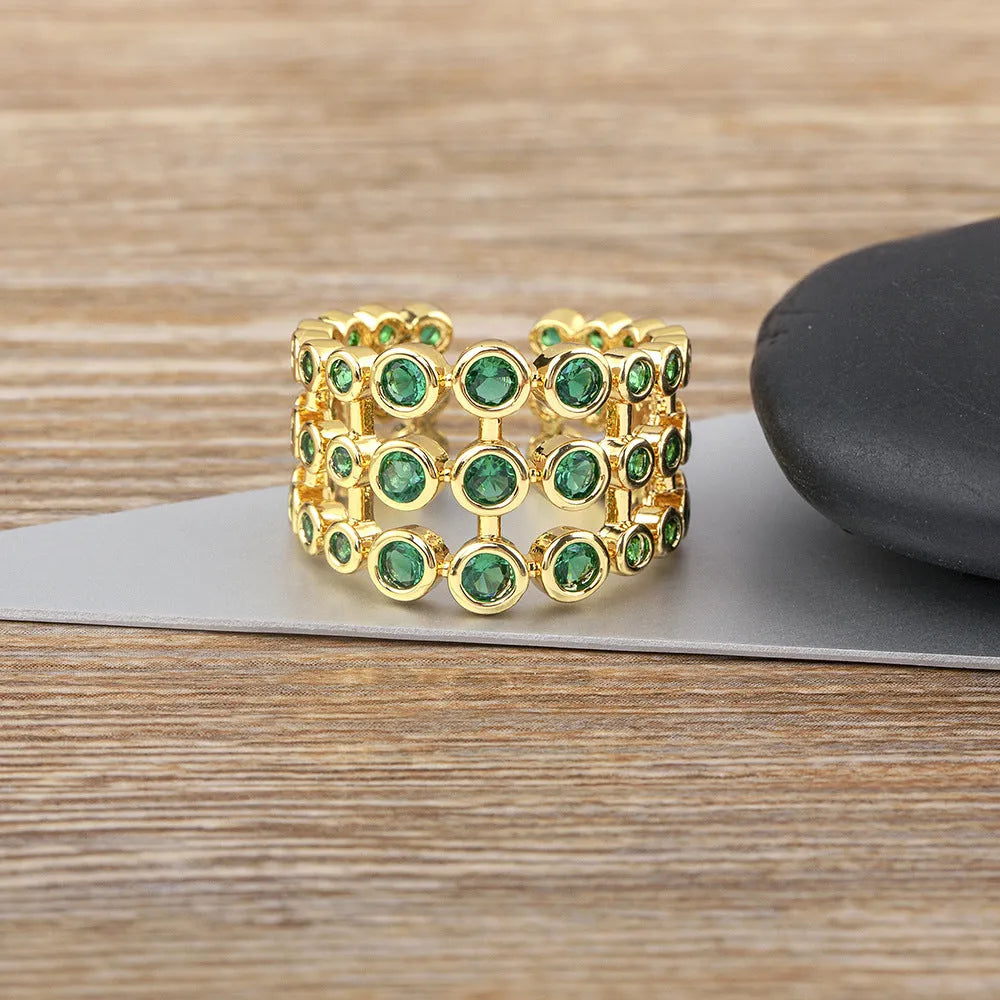Gold coloured copper ring with green zircon stones set across its wide, layered band.