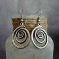 Silver geometric spiral earrings with a distressed texture on a white background.