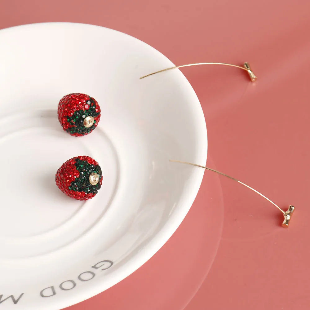 Close-up of women's geometric strawberry-shaped earrings with spot drill texture, on a red background.