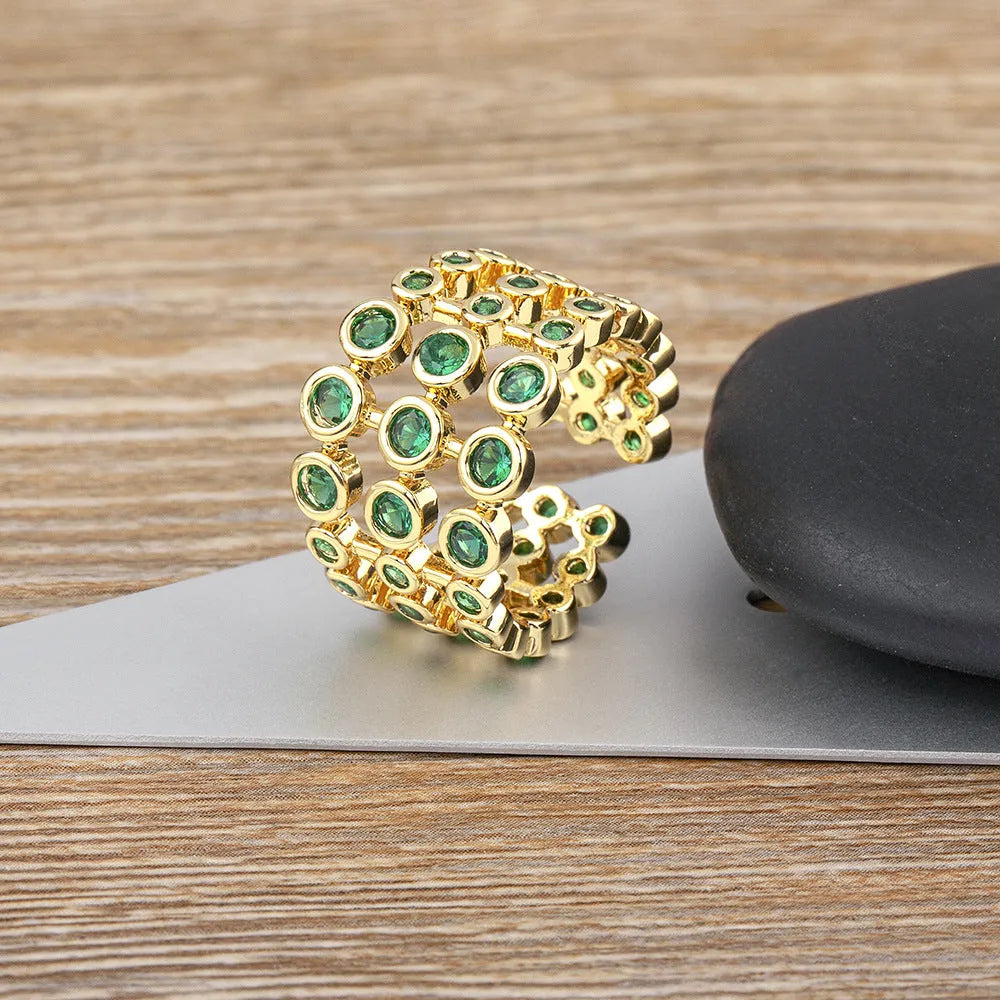 Gold coloured copper ring with green zircon stones set across its wide, layered band.