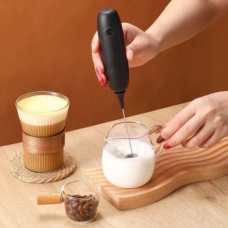 Handheld electric milk frother blender in black and white colour options on a kitchen counter.